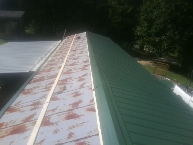 Old rusted panels beside newly installed green metal roofing — Wind Damage Roof Repair by Roofing Brothers in Deadwood
