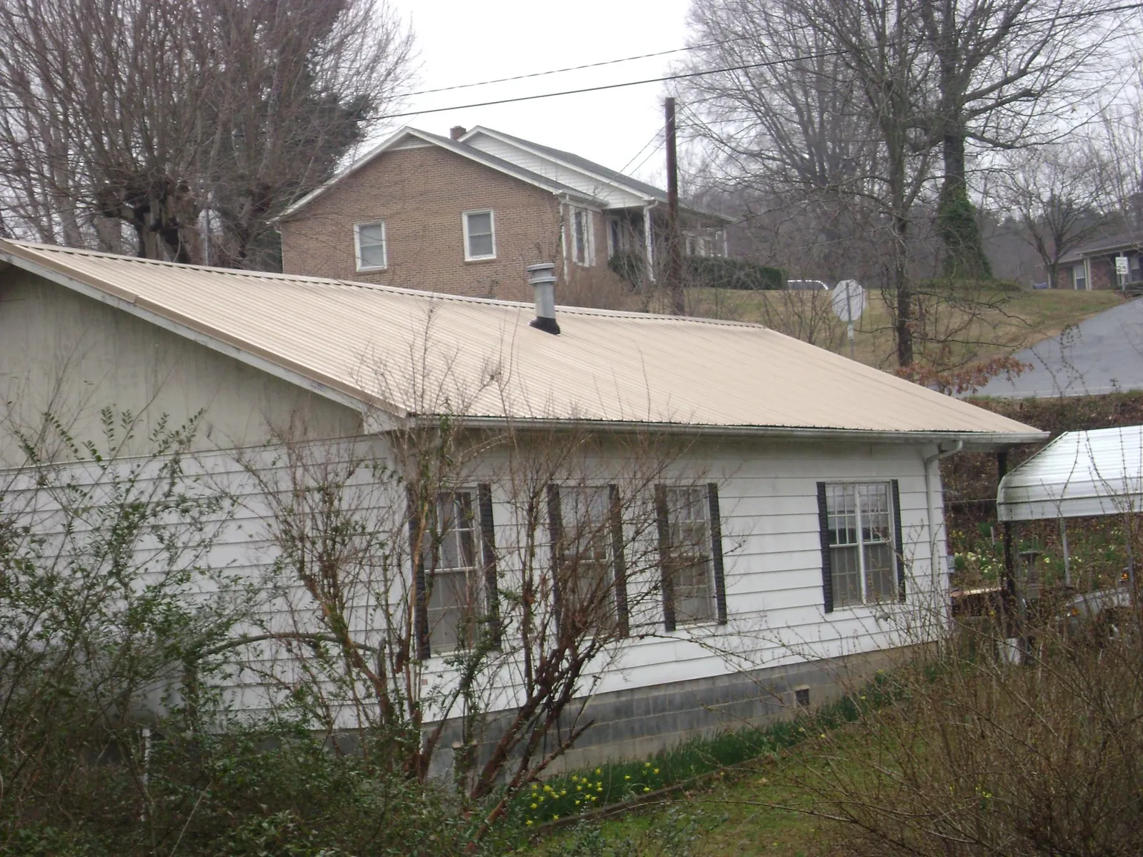 Tan metal roof on a white sided house set into a hillside — Commercial Roofing by Roofing Brothers in Deadwood