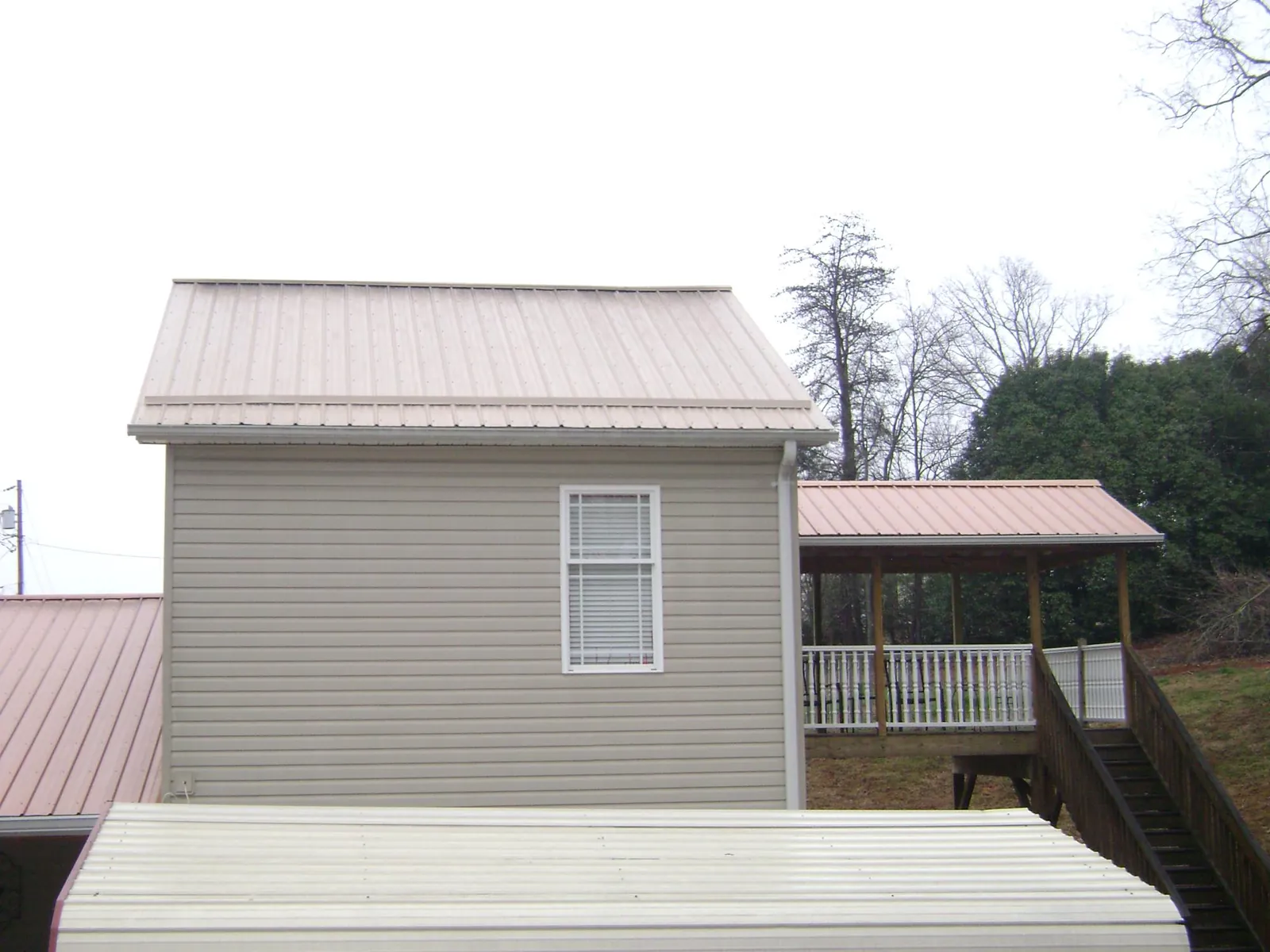 Tan metal roofs on a two story addition and attached porch, from a Roof Replacement job in Deadwood